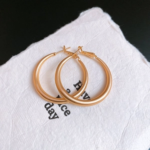 Macro view of matte gold C-shaped hoop earrings on white paper with minimal text