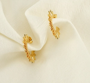 Macro shot of gold C-shaped earrings with radial sunburst design on textured fabric