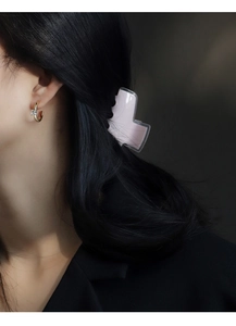 Close-up of a gold C-shaped earring with square zircon and a pink butterfly hair claw