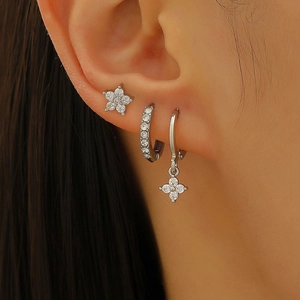 Close-up of silver earrings set with zircon star and flower motifs on a model's ear