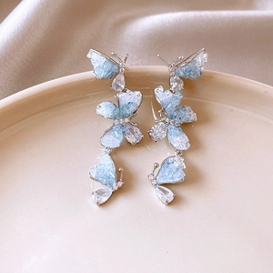 Close-up of butterfly drop earrings with blue crystal stones on a ceramic plate