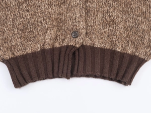 Detailed close-up of brown chunky knit fabric with ribbed hem and dark round button
