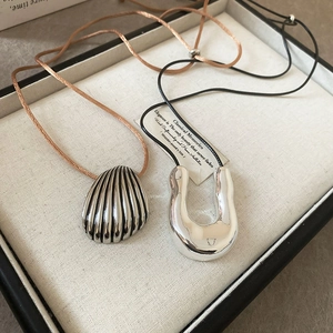 Macro shot of silver shell pendant and U-shaped metal necklace on beige jewelry tray