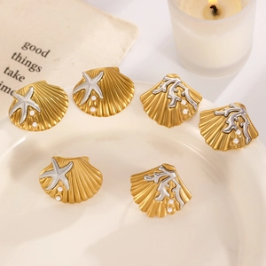 Golden shell earrings set with starfish, coral, and pearls on a ceramic tray