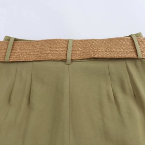 Detail view of olive casual shorts featuring a woven straw belt and pleated waist design