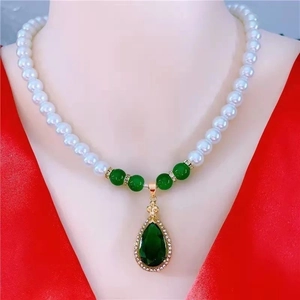 Elegant pearl necklace with green emerald teardrop pendant on a red silk background