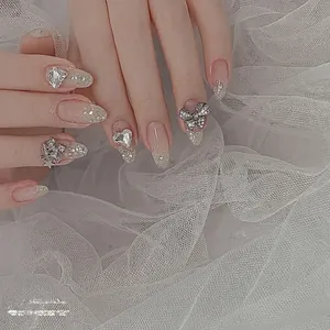 Nail art avec nœuds argentés et strass en cœur sur faux ongles amande scintillants