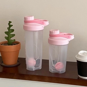 Pink protein shaker bottles with mixing balls on a wooden window sill with plants