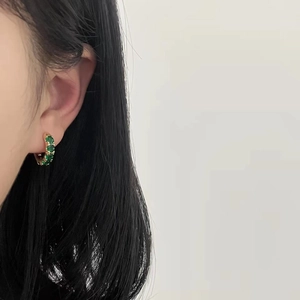 Close-up of elegant gold C-shaped earrings with green zircon stones worn by a model