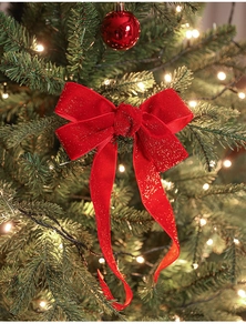 Red velvet Christmas bow with gold glitter on a green tree with warm lights