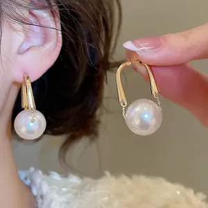 Elegant U-shaped gold pearl earrings with round white pearls and minimalist metallic finish