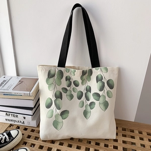 Minimalist canvas tote bag with green eucalyptus leaf print and black handles on wood stool