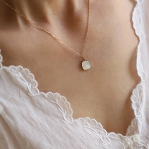 Macro detail of a gold square shell pendant necklace with sunburst patterns on a model