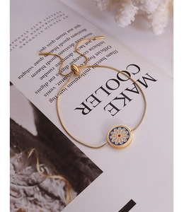Detail of 18K gold-plated snake chain bracelet with blue enamel daisy charm on magazine