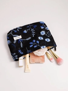 Linen makeup bag with blue flower embroidery and cosmetics shown from a 45-degree angle