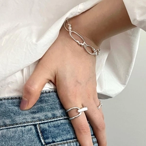 Detail of silver chain bracelet and geometric ring worn by model in minimalist casual style