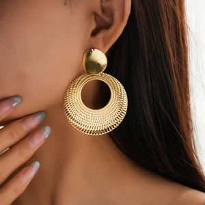 Close-up of model wearing gold metallic hollow round hoop earrings with textured engraving