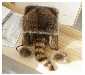 Detail of winter raccoon style faux fur hat with long striped tail and fuzzy pom-poms