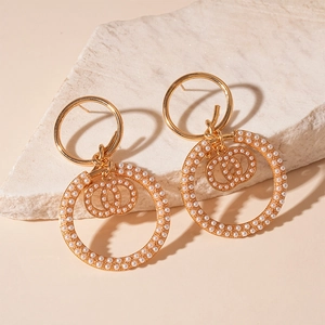 Elegant gold knotted pearl hoop earrings featuring double-C logo on white stone background