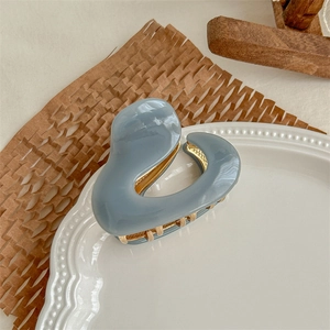 Close-up of a glossy blue acetate hair claw clip with golden metal teeth on a white plate