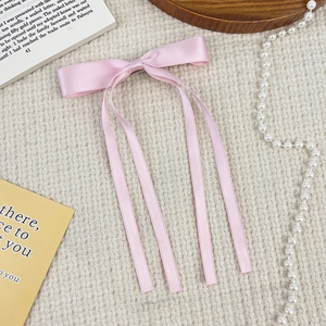 Detail of pink silk ribbon bow hair clip with long streamers on beige background