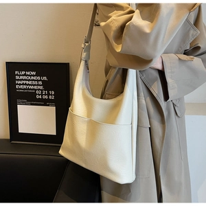 Side view of a beige large-capacity bucket bag styled with a classic khaki trench coat
