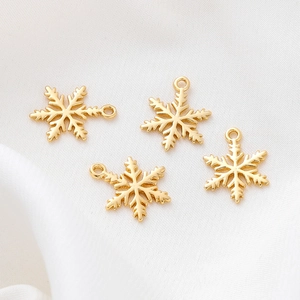 Detailed view of four 18K gold-plated snowflake charms on soft white fabric background