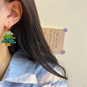 Close-up of handmade beaded Christmas tree earrings with red bow and crystal details