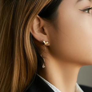 Close-up of gold heart earrings with wavy metal drop and pear-shaped zircon stone