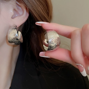 Silver C-shaped metal stud earrings with hammer texture shown on model in side profile view