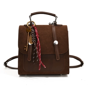 Brown faux suede backpack with vintage key charm and decorative braided ropes on white background