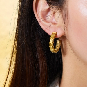 Détail des boucles d'oreilles créoles dorées texture bambou portées par un modèle