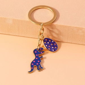 Close-up of golden metal keychain featuring blue dinosaur pendant and colorful polka dot egg