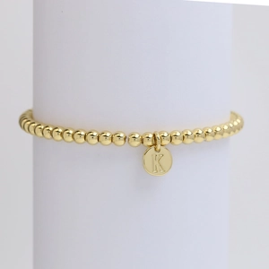 Macro detail of golden beaded bracelet featuring a round pendant engraved with letter K