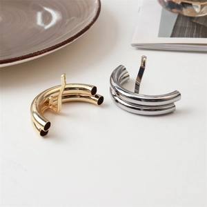 Detailed close-up of minimalist gold and silver cylindrical metal hair clips on white surface