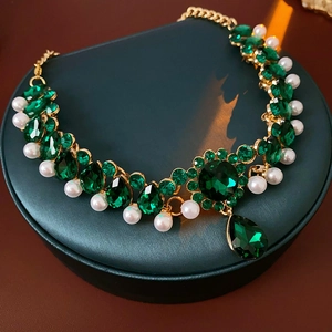 Close-up of vintage gold necklace with green gemstones and white pearls on leather