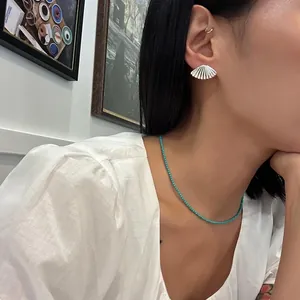 Close-up of a silver fan-shaped earring and turquoise beaded necklace on a model