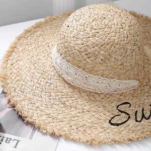 Detailed macro view of beige raffia straw hat with white lace ribbon and Sun embroidery