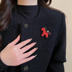 Nahaufnahme einer roten perlenbesetzten Pferde-Brosche an einer schwarzen Tweed-Jacke