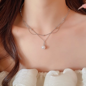 Détail d'un collier argenté à double épaisseur avec petites billes et un pendentif perle