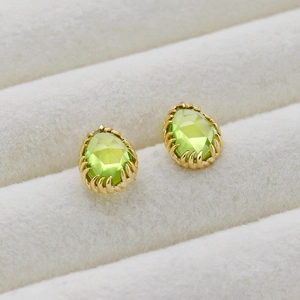 Macro shot of green teardrop earrings with gold serrated settings on beige velvet