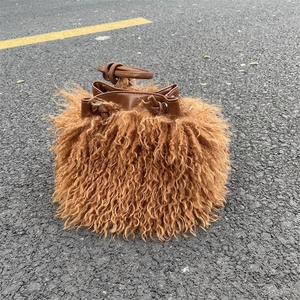 Brown faux sheepskin plush bucket bag with drawstring and leather handles on asphalt