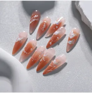 Detailed view of stiletto press-on nails with orange gradient, pearls and butterfly motifs