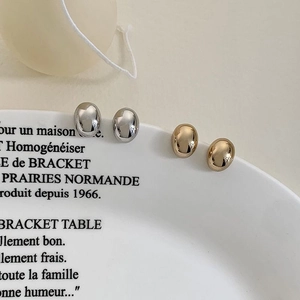 Detail of gold and silver minimalist oval stud earrings on white ceramic plate
