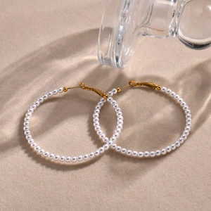 Detail shot of gold C-shaped hoop earrings with small pearls on beige velvet background