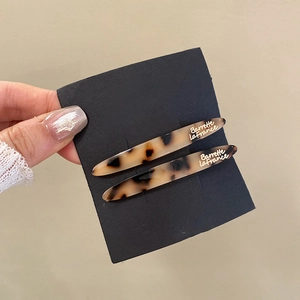 Close-up of tortoise shell pattern hair clips with golden lettering on beige background