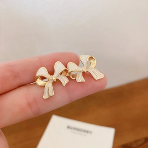 Primo piano di eleganti orecchini a fiocco in smalto bianco placcato oro sulle dita