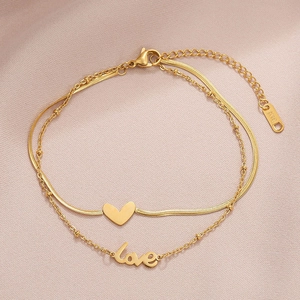 Detail of 18K gold-plated double-layer anklet with heart and love pendants on pink fabric