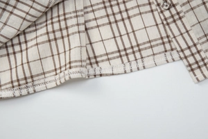 Detailed macro view of brown plaid fabric texture and fine hem stitching on casual shirt
