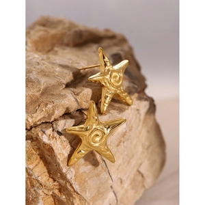 Close-up of golden starfish earrings resting on a natural light brown textured stone